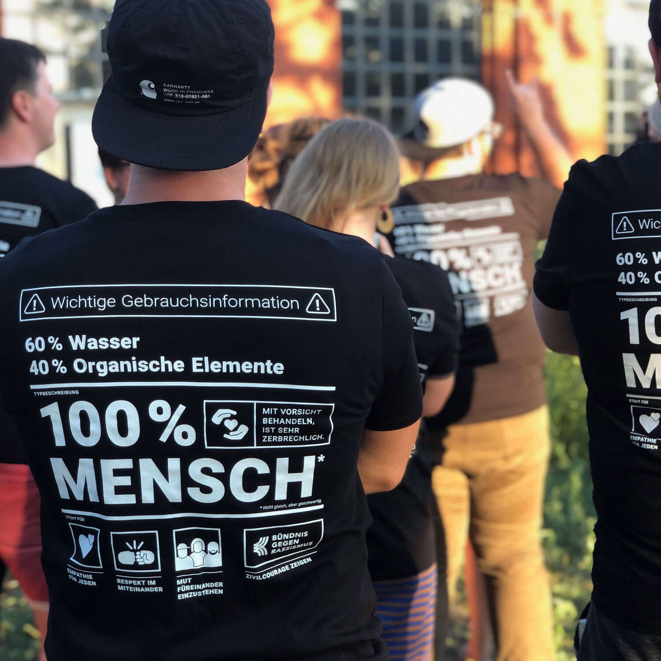 Eine Person von hinten ist zu sehen. Sie trägt ein Shirt mit der Botschaft 100% Mensch